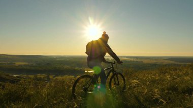 Bisikletçi sabah güneş doğarken parktaki dağın tepesinde seyahat eder. Özgür genç adam bisikletini tepenin kenarına sürüyor ve güneşin ve doğanın tadını çıkarıyor. Mutlu gezginler bisikletle