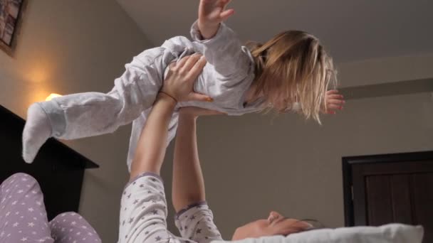 Genç bir anne, evdeki kanepede uçakla oynayan tatlı bir kızı kucağına alıyor. Mutlu bir aile. Bir çocuk, bir kız, oynuyor, gülüyor ve annesinin kollarında uçuyor. Aile sabahları birlikte jimnastik yapıyor. — Stok video