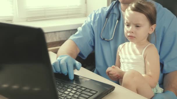 Niña paciente se sienta en la falda de pediatría. concepto de examen pediátrico para el tratamiento de niños. Cuidado médico pediatra profesional, jugando con un niño preescolar lindo y trabajando en el ordenador portátil — Vídeos de Stock