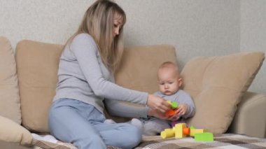 Bebek ve anne birlikte kanepede renkli küplerle oynuyorlar. Mutlu bir aile. Anne çocuklarının motor becerilerini geliştirir. Bir çocuğa oyun oynayarak öğretmek. Çocuklar için eğitici oyunlar