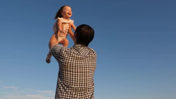 Child plays and wants to fly like an airplane. Dad throws his happy daughter into blue sky. Family travel. Father and little child play, laugh, hug together. Family walking in park in summer, weekend — Stock Video