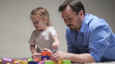 Bir çocuk, bir kız ve bir baba aile evi inşa ediyorlar. Mutlu bir aile. Çocuklar için eğitici oyunlar. Baba ve kızı çocuk odasında yerde renkli küplerle oynuyorlar. Çocuğa oyun aktiviteleri yoluyla öğretmek