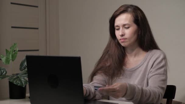 Una mujer en casa está sentada a la mesa en la sala de estar, usando una computadora, comprando en una tienda en línea, disfrutando del trato. Freelancer trabaja remotamente desde casa. Mujer de negocios trabaja para una computadora portátil en línea. — Vídeos de Stock