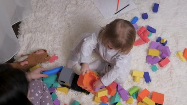Дитина, дівчинка, мама грають у барвисті іграшкові кубики та іграшкові машини в дитячій кімнаті. Освітні ігри для розвитку дітей. Навчання дитини за допомогою ігрової діяльності. Мати і дитина грають — стокове відео