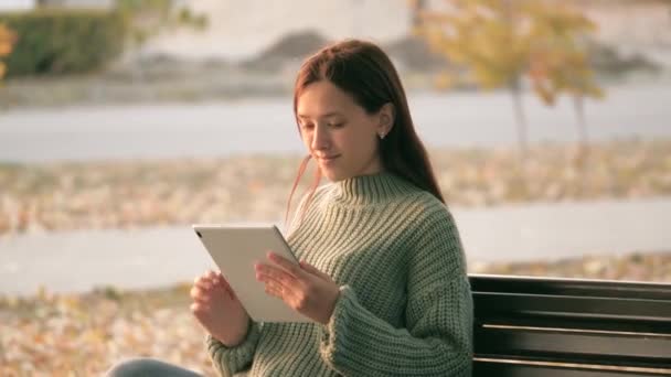 Wanita muda bekerja pada tablet di taman di bangku cadangan. Seorang gadis menggunakan tablet digital mencetak pesan di jalan kota. Siswa perempuan belajar dengan komputer tablet di luar ruangan. Pekerja lepas bekerja secara online. — Stok Video