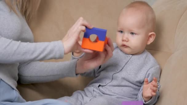 Madre e hijo juegan juntos en cubos de colores infantiles en el sofá en la sala de estar. Familia feliz. Mamá desarrolla habilidades motoras infantiles. Enseñar a un niño a través del juego. Juegos educativos para niños — Vídeo de stock