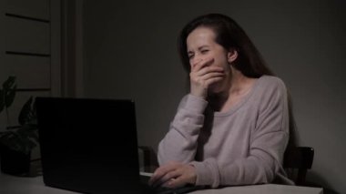 Geceleri evdeki bir kadın modern bir bilgisayarda uzaktan çalışıyor. Dizüstü bilgisayarda yazı yazan yorgun bir iş kadını. Bilgisayarda çalışan serbest çalışan bir kadın. Kadın masada oturuyor, kanalda çalışıyor..