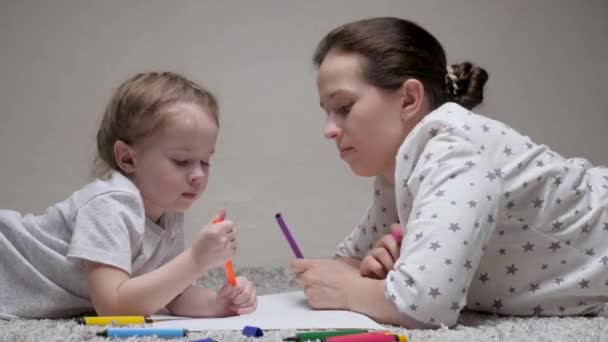 Criança e mãe, babá, ensina menina a desenhar. Família feliz brincando juntos em casa no chão. Uma mãe ajuda sua filha a aprender a desenhar em papel, colorir com lápis multicoloridos e canetas de feltro. — Vídeo de Stock