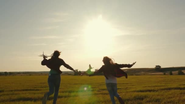 Children on background of sun with an airplane in hand. Dreams of flying. Happy childhood concept. Two girls play with a toy plane at sunset. Silhouette of children playing on the plane — Stock Video