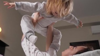 A child and a young mother play an airplane together on the couch at home, dreams of flying. Happy family. A kid, a girl, plays, laughs and flies on plane in her mothers arms. Family doing gymnastics