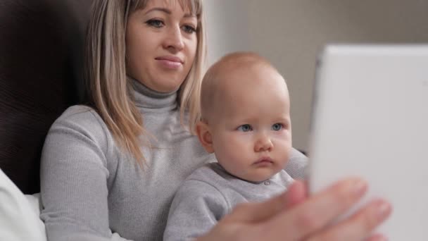 Happy family, parent, mother and little child, son, daughter, having fun using a digital tablet, lying on bed at home. Baby, toddler, girl, boy , child learning, looking at tablet screen at home. — Stok video