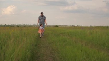 Happy family, dad and little daughter are playing, father catches up with child in park on green grass. Dad and baby are happy to run and walk outdoors. Dad walks with his beloved daughter at weekend.