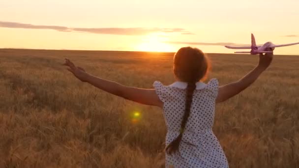 Avion dans la main d'une fillette courant dans un champ de blé vers le soleil. Aviateur fille, rêves et fantasmes sur le vol. Bonne enfance. Rêves adolescents de voler sur les avions et le monde du voyage. — Video