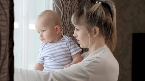 Mother, child, daughter, play and look out into the street, accompanying the father. Infant and mommy. Happy family. Kid son and young mom are playing looking out the window together waiting for dad.