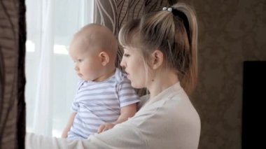 Anne, çocuk, kız, oyun oynayın ve sokağa bakın, babaya eşlik edin. Bebek ve anne. Mutlu bir aile. Küçük oğul ve genç anne birlikte pencereden dışarı bakıp babalarını bekliyorlar..