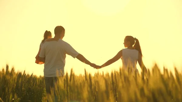 Sağlıklı anne, baba ve küçük kız birlikte doğanın tadını çıkarıyorlar. Çocuklu mutlu çiftçi ailesi buğday tarlasında yürüyor. Ağır çekim. Anne, baba ve çocuk el ele yürüyorlar.