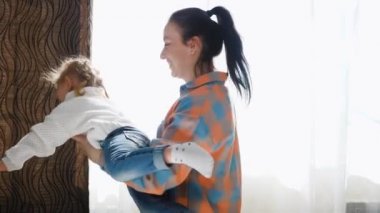 Anne çocuğuyla oynuyor, kızı kollarında daireler çiziyor, tatlı bebek mutlu ve evde gülüyor. Bebek ve anne evde oynuyorlar. Sevimli bir kız zevkle uçar ve annesiyle oynar..