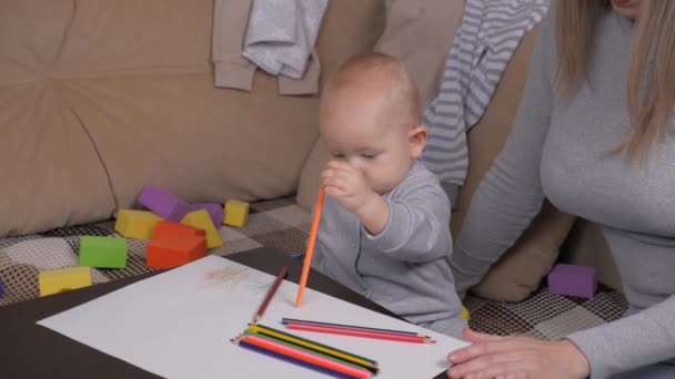 Μια μικρή κόρη ζωγραφίζει με ενθουσιασμό με χρωματιστά μολύβια σε χαρτί, ένα κοριτσάκι δίπλα στη μητέρα της. Μικρέ, ο γιος ζωγραφίζει με χρωματιστά μολύβια, το αγόρι είναι σπίτι με τη μητέρα του. Οικογένεια και — Αρχείο Βίντεο