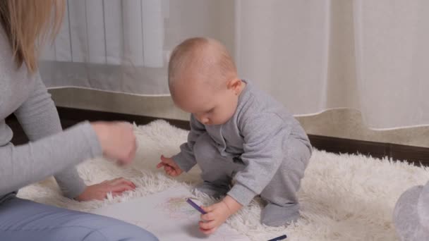 Una bambina disegna con entusiasmo con la matita gialla su un foglio di carta, una bambina accanto a sua madre. Famiglia felice e bambino. Ragazzo, il figlio disegna con matite colorate, il ragazzo è a casa con sua madre — Video Stock