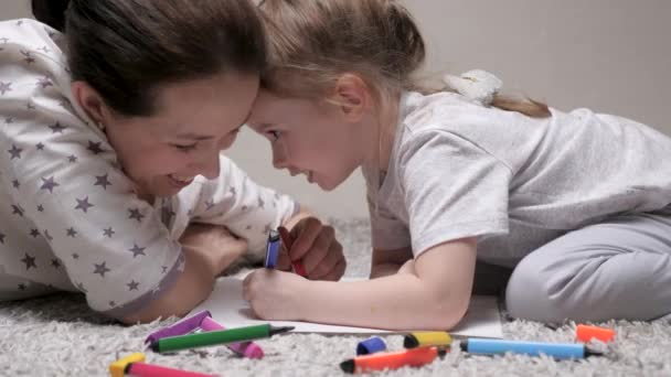 Çocuk ve anne, dadı, kıza resim yapmayı öğretiyor. Mutlu aile evde yerde birlikte oynuyor. Bir anne kızına kağıt üzerinde resim yapmayı öğrenmesine yardım eder. Renkli kalemler ve keçeli kalemlerle boyama yapar.. — Stok video