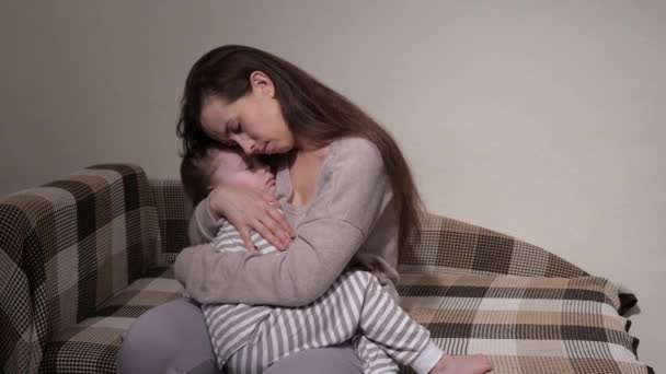 Yorgun anne uyuyan bebeğini kollarında tutuyor. Çocuk güzel rüyalar görüyor. Anne sevgili kızını yatağına yatırır. Geceleri mutlu bir aile. Anne ve bebek kanepede birlikte dinleniyorlar. Sağlıklı çocukluk — Stok video