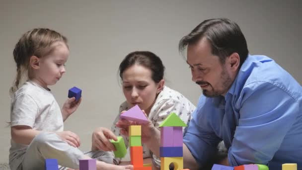 Criança, pai e mãe estão construindo uma casa de família. Família feliz. Jogos educativos para crianças. Pai e mãe filha jogar cubos no berçário no chão. Ensinar a criança através de atividades lúdicas — Vídeo de Stock