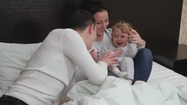 Los padres jóvenes juegan con un niño pequeño. Familia feliz, niño, hija mamá papá jugar remo juntos en la habitación en la cama. Niño, madre escondida bajo las sábanas, papá juega a buscar. Familia riendo mientras juega juego — Vídeo de stock