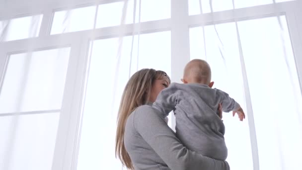 Bambino figlio e giovane mamma stanno giocando guardando fuori dalla finestra insieme in attesa di papà. Una famiglia felice. Madre, figlia, figlia, gioca e guarda in strada, accompagnando il padre. Bambino e mamma. — Video Stock