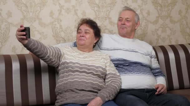 Szczęśliwe małżeństwa w średnim wieku są fotografowane na smartfonie, selfie razem w domu. Szczęśliwa rodzina. Starsza, dojrzała para kręci filmy i zdjęcia na nowoczesnym smartfonie. — Wideo stockowe