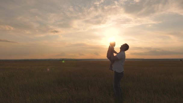 Babam gün batımında mutlu kızını gökyüzüne fırlatıyor. Baba ve küçük bir çocuk sahada birlikte oynuyorlar, gülüyorlar ve sarılıyorlar. Aile seyahati. Çocuk ebeveynin kollarında. Baba günü izinli. Mutlu aile ve çocukluk — Stok video