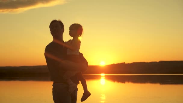 Feliz família pai e bebê, filha abraçando no lago ao pôr-do-sol. Pai e criança ao sol. Conceito de sonho de infância. Família feliz menina e pai sozinho com a natureza descansar no parque de verão — Vídeo de Stock