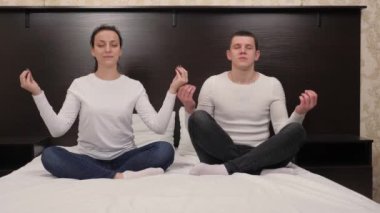 Birbirine aşık genç erkekler ve kadınlar yatakta meditasyon yapar, evde yoga yaparlar. Mutlu genç aile nefes egzersizleri yapıyor, evde meditasyon yapıyor. Spor konsepti. Sağlıklı bir yaşam tarzı.