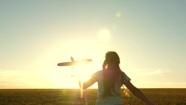 Ragazza felice corre con un aeroplano giocattolo su un campo alla luce del tramonto. i bambini giocano aereo giocattolo. adolescente sogna di volare e diventare pilota. la ragazza vuole diventare pilota e astronauta. Rallentatore — Video Stock