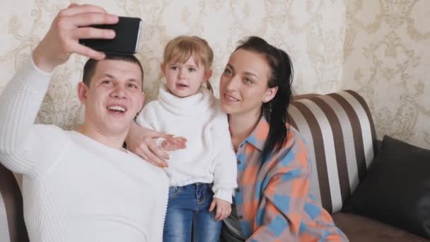 Mother, father, baby, daughter bloggers in room communicate using a modern gadget online. Happy young family with child, girl waving to friends while talking during smartphone video call at home. — Stock Video