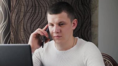 Modern dizüstü bilgisayar ve cep telefonuyla çalışan serbest çalışan biri. İş adamı, dizüstü bilgisayarla çalışıyor, akıllı telefonla konuşuyor. Ofiste, evde bilgisayar ve cep telefonu kullanan profesyonel bir erkek..
