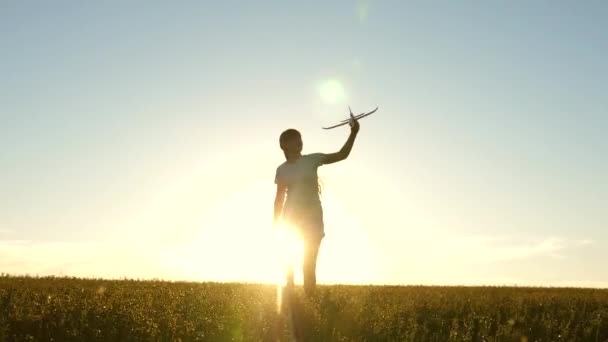 Menina feliz corre com um avião de brinquedo em um campo sob a luz do pôr do sol. As crianças brincam de avião de brinquedo. sonho adolescente de voar e se tornar piloto. a menina quer se tornar piloto e astronauta. Movimento lento — Vídeo de Stock