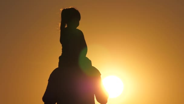 Daughter, daddy play together in sunshine. Silhouette of dad carries beloved child on his shoulders. A father walks with his daughter on his shoulders at sunset. Kid walks with dad. Happy family — Stock Video