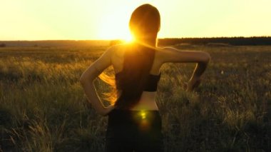 Özgür genç bir kadın gün batımında yaz parkında spor yapmaya gider. Sağlıklı, güzel bir kız şehrin dışında güneşlenir. Dışarıda antrenman ve ısınma egzersizleri. Kız sahada temiz hava soluyor..