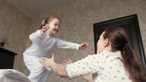 Šťastná dcera vyskočí z postele ke své matce v náručí a obejme ji. Matka si ráno hraje se svým dítětem. Rodina se doma baví. Aktivní rodinná dovolená doma. Šťastné a zdravé dětství — Stock video