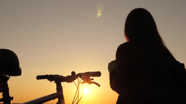 Donna felice ciclista a riposo nel parco. Giovane escursionista libera si trova sulla collina accanto alla bicicletta godendo la natura e il sole. Ragazza libera viaggia in bicicletta al tramonto. Avventura e concetto di viaggio — Video Stock