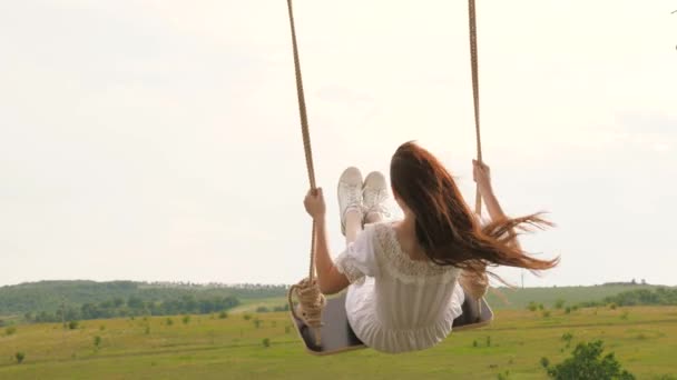 Wooden swing with swinging free, happy woman outdoors. Swing on a swing, dreams of flying. A young girl in dress swinging on swing in evening park. Travel in spring summer in nature. Healthy lifestyle — Stock Video