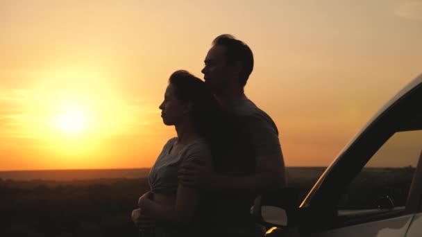 Les amoureux heureux voyagent en voiture. Un homme et une femme s'embrassent près de la voiture et admirent le magnifique coucher de soleil au camping. Les touristes voyagent en voiture, admirent le lever du soleil, la nature. Voyageurs gratuits, touristes. Voyage en famille en voiture. — Video