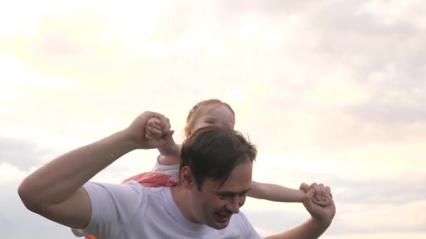 Papa en dochter spelen vrolijk samen in de open lucht. Vader draagt schouders van zijn geliefde kind voor de hemel. Papa en kind spelen vliegtuig van dromen om te vliegen. Gelukkige familie rust in het park. — Stockvideo