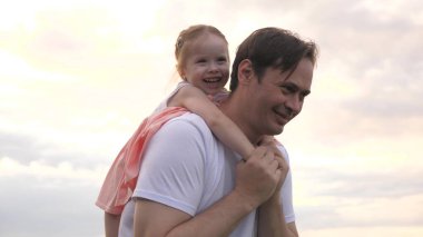 Baba ve kızı açık havada neşeyle oynuyorlar. Baba, sevgili çocuğunun omuzlarını gökyüzünün önünde taşıyor. Baba ve çocuk uçma hayalleri oynuyorlar. Mutlu aile parkta dinleniyor..