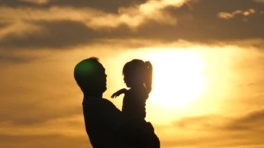 Baba, küçük çocuk, Doka oynuyor, gülüyor, gökyüzünün önünde sarılıyorlar. Bebek silueti, baba. Babası mutlu kızını gökyüzüne fırlattı. Aile seyahati. Bebek ebeveynin kollarında. Babam izinli. Mutlu aile.