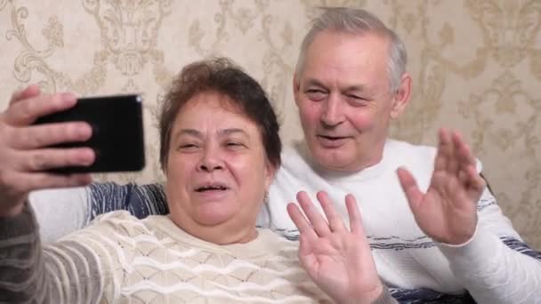 Una pareja de ancianos, casados yloggers en línea disparar vídeos y fotos en el teléfono inteligente moderno. Familia feliz. Felices parejas casadas de mediana edad son fotografiados en un teléfono inteligente, tomar selfies juntos en casa — Vídeo de stock