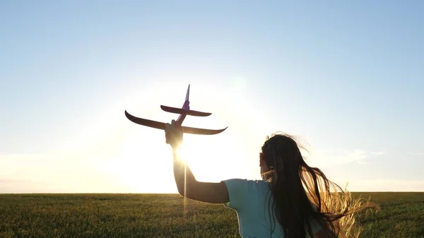 Lycklig flicka springer med leksaksflygplan över fältet i solnedgångens strålar. Barnen leker i leksaksflygplan. Tonåringen drömmer om att flyga och bli pilot. Flickan vill bli pilot och astronaut. Långsamma rörelser — Stockfoto