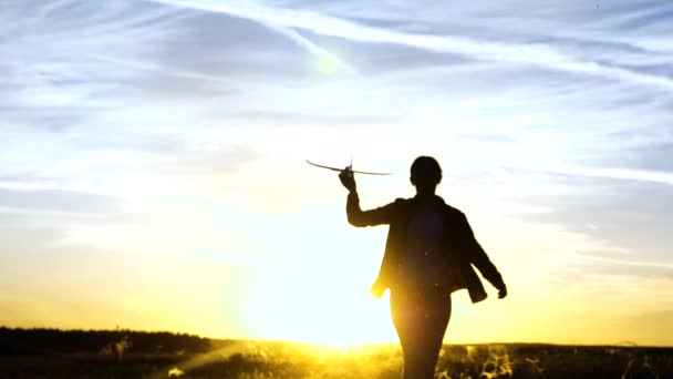 Menina feliz corre com um avião de brinquedo em um campo na luz do pôr do sol. A rapariga quer tornar-se piloto e astronauta. Movimento lento. As crianças brincam de avião de brinquedo. Sonhos adolescentes de voar e se tornar piloto. — Vídeo de Stock