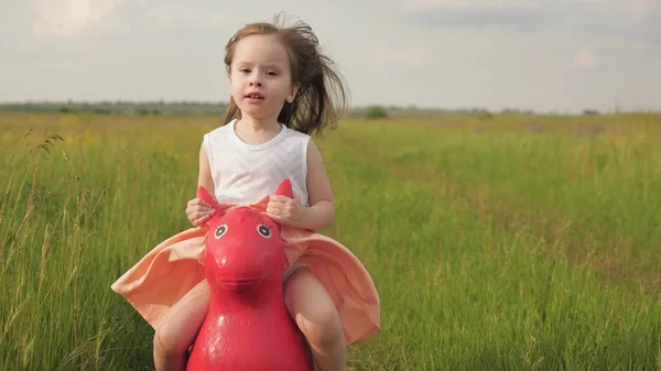 Счастливая маленькая девочка играет в парке и прыгает на надувном игрушечном осле. Парень играет в поле со своей любимой игрушечной лошадью. Маленькая девочка, дочь играет на улице. Семья и детство. — стоковое фото