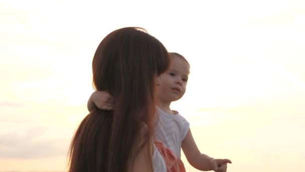 Mom, cute baby walk together in park and hug in sun. Happy family, mom, daughter are playing at sunset. Mom, child are walking in front of sky. Happy family, healthy childhood. Family walking in park — Stock Video